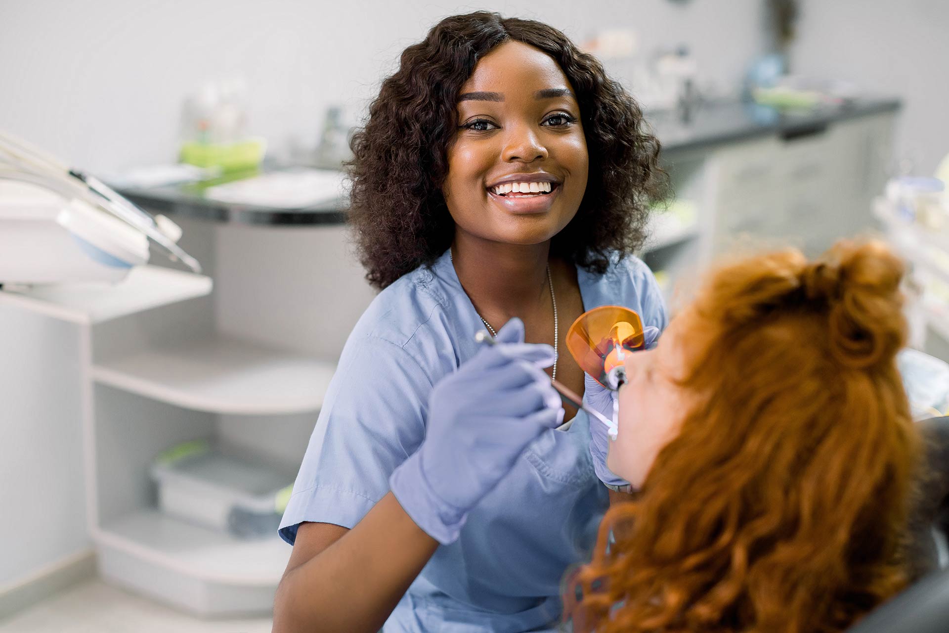 Dental hygienist smiles at camera while working with patient