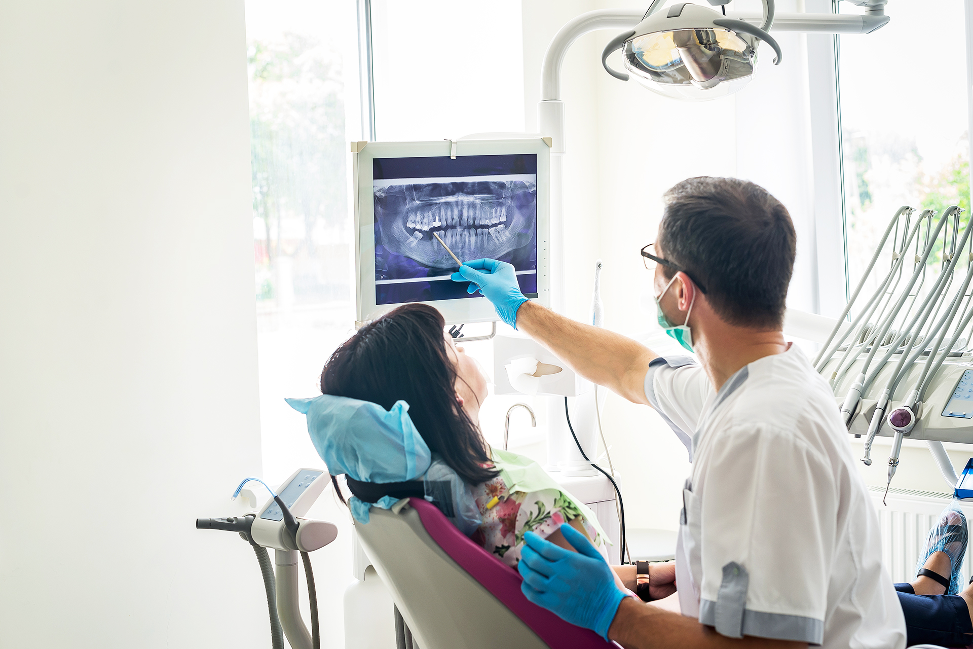 Dentist pointing to x-ray machine with patient in the chair