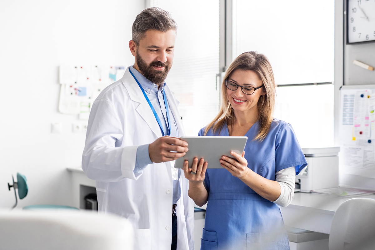 A dentist and dental assistant reviewing applications on a tablet.