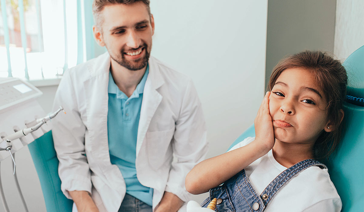 little girl showing toothache in dental chair with dentist