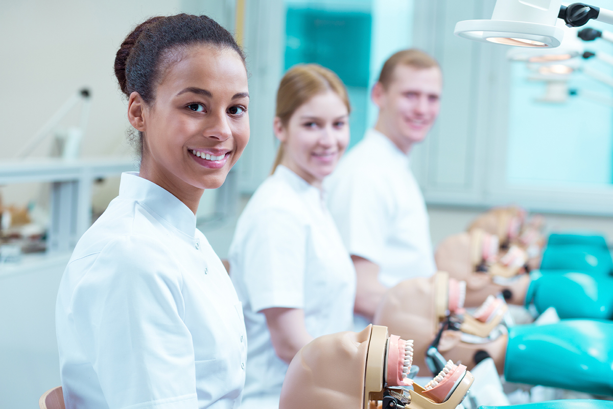 Three smiling dental students in class working with training manikins.