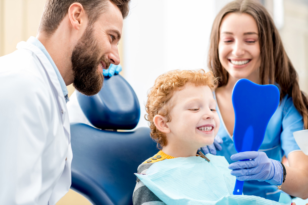 dentist and dental assistant showing child patient a mirror to look at his teeth