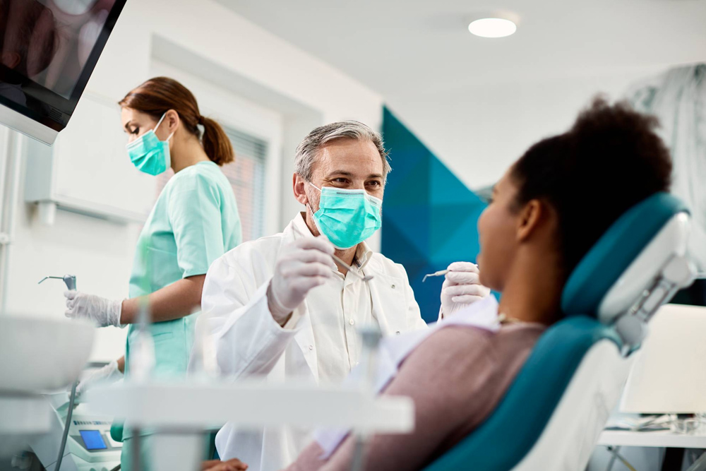 Dentist with face mask talking to patient during procedure at dental clinic